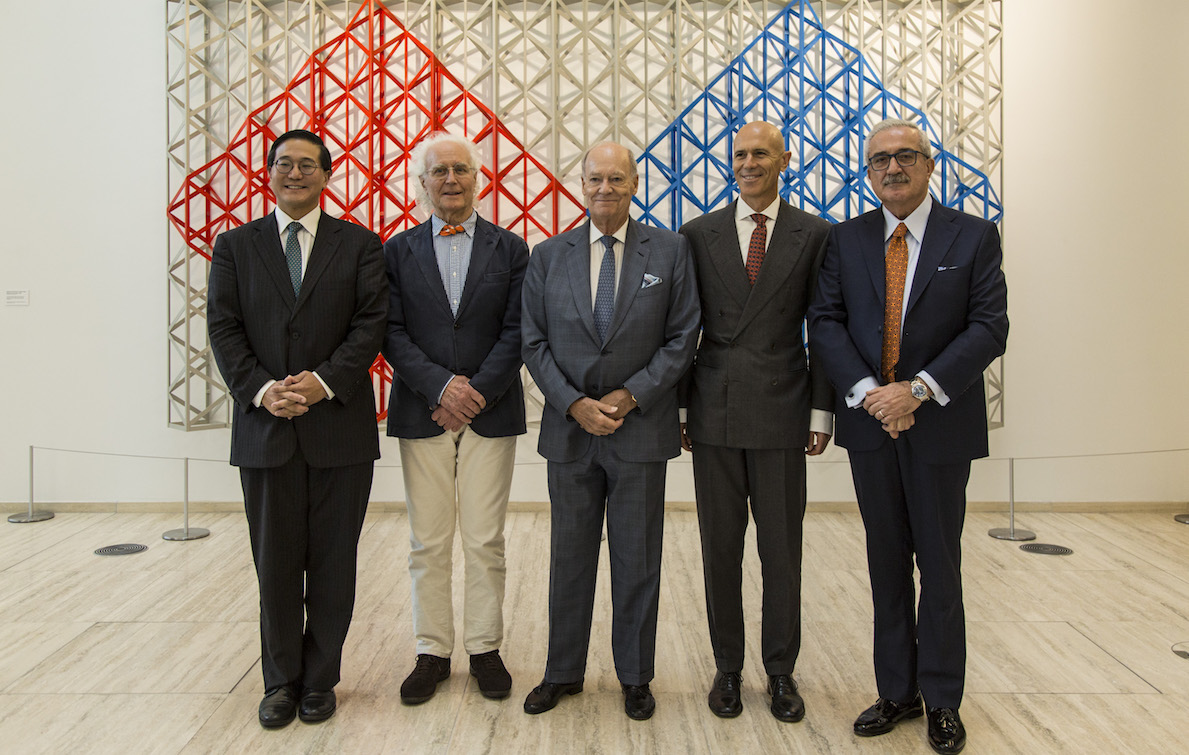 6 older men dressed in suits standing in front of an art piece